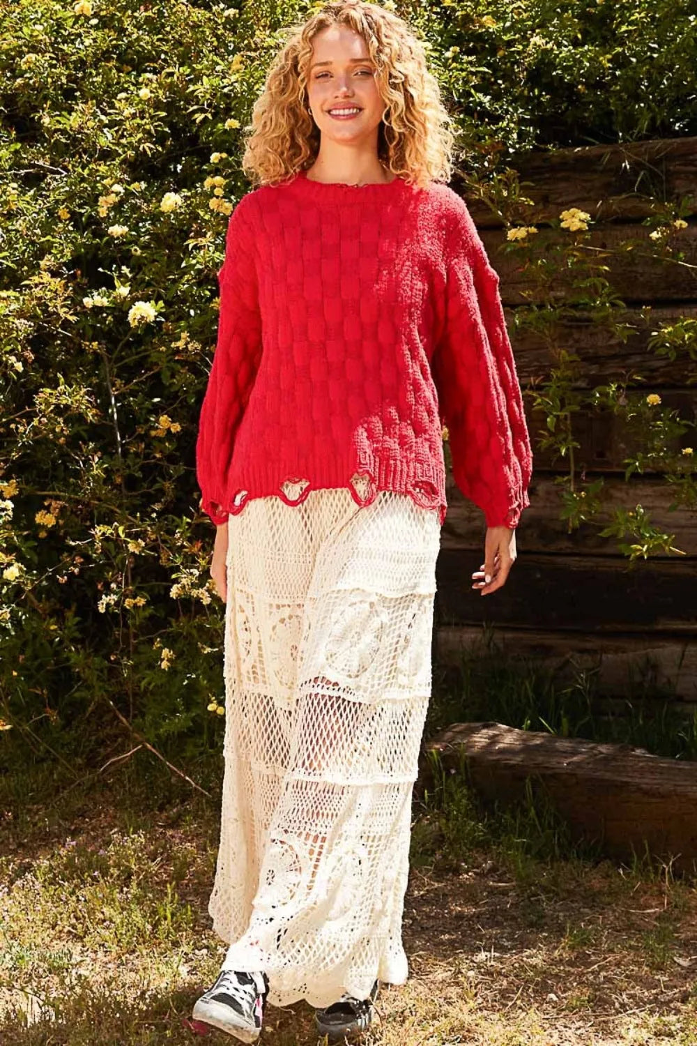 Woman wearing a boho checkered distressed sweater with balloon sleeves, paired with white lace pants