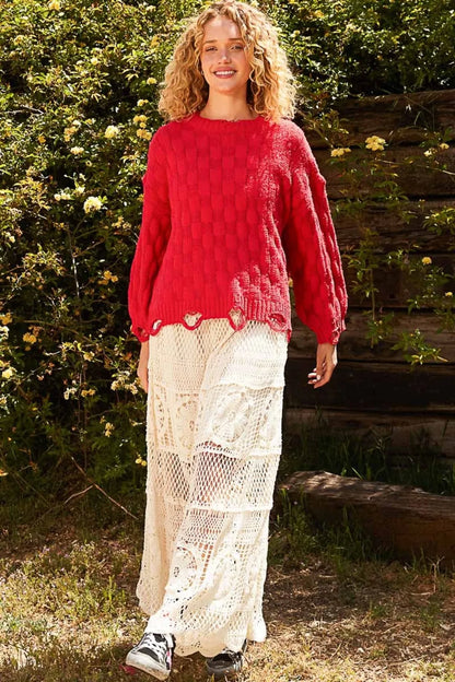 Woman wearing a boho checkered distressed sweater with balloon sleeves, paired with white lace pants