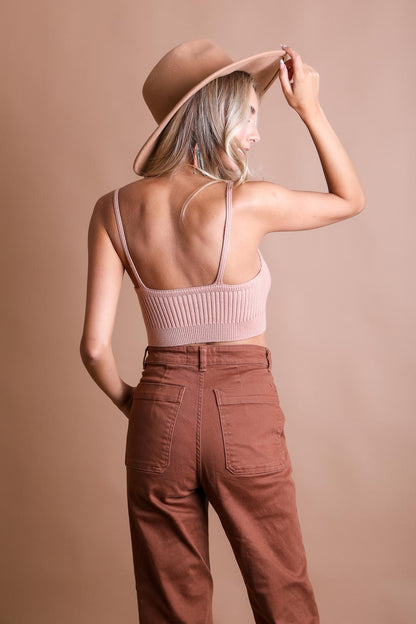 Woman wearing a rib knit lounge brami in soft pink with high-waisted pants and a stylish hat
