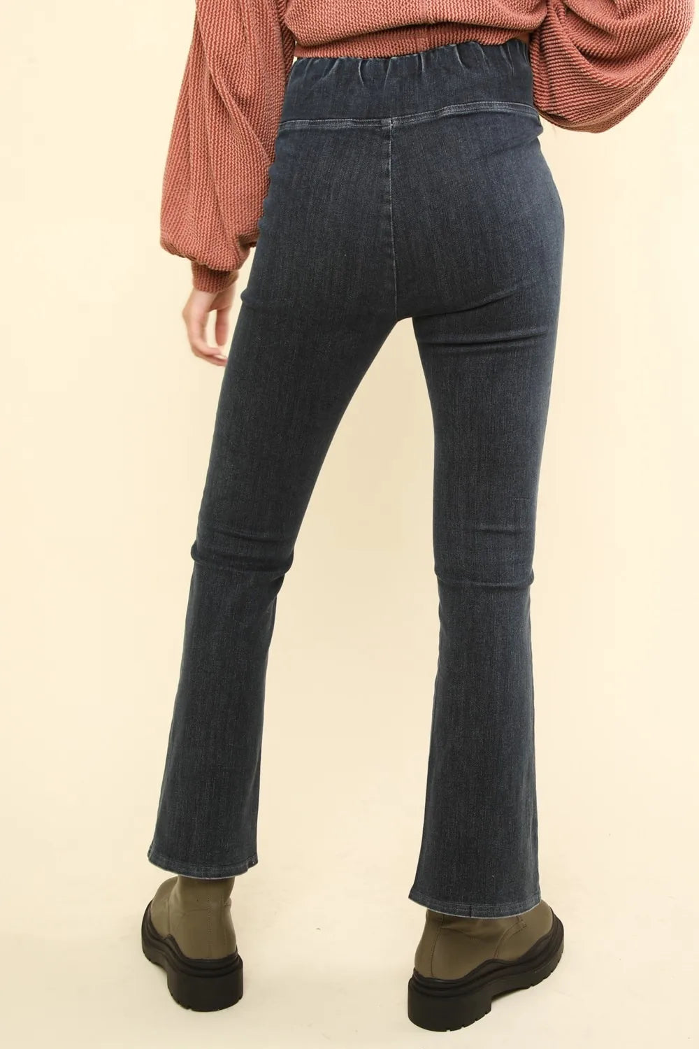 Back view of crossover waist denim leggings in dark wash with a flared hem for a stylish look