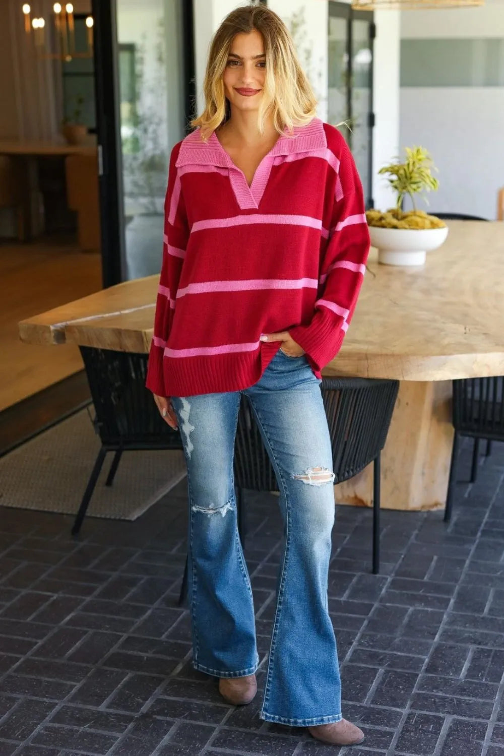 Casual model wearing a collared striped boho sweater in pink and red with flared jeans