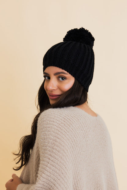 Stylish woman wearing a black chunky cable knit pom beanie for cozy winter fashion