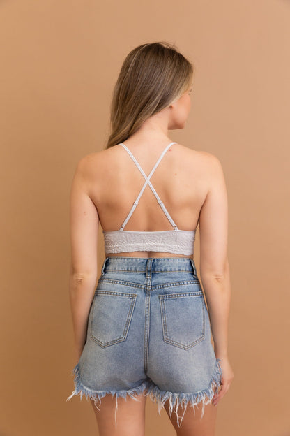 Back view of a woman wearing a floral jacquard bralette with crisscross straps and denim shorts