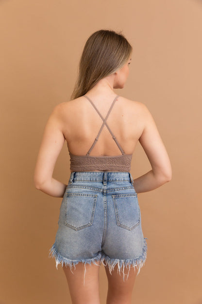 Model wearing a floral jacquard bralette with crisscross straps and distressed denim shorts