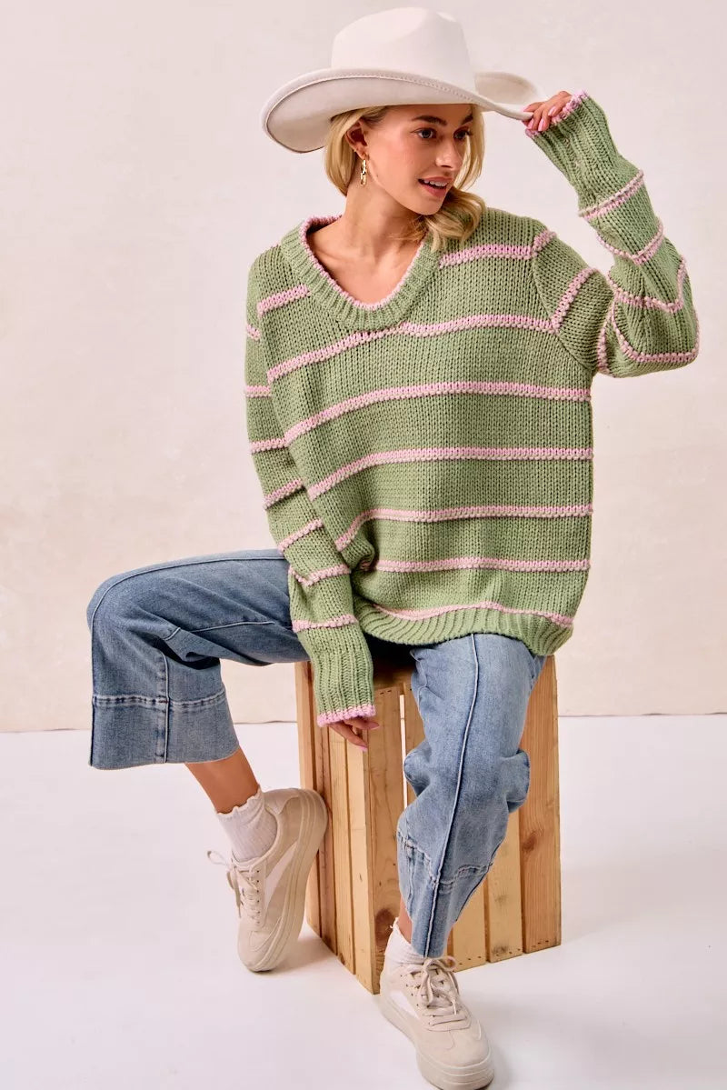 Model wearing a boho striped long sleeve sweater in green, paired with jeans and a hat for a casual look