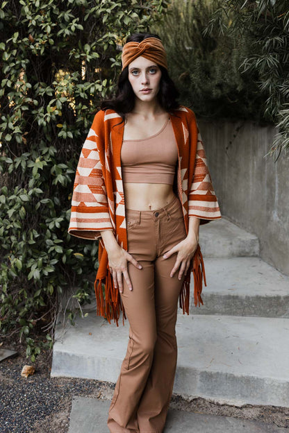 Stylish model wearing an Aztec print fringed ruana over a crop top and flared pants