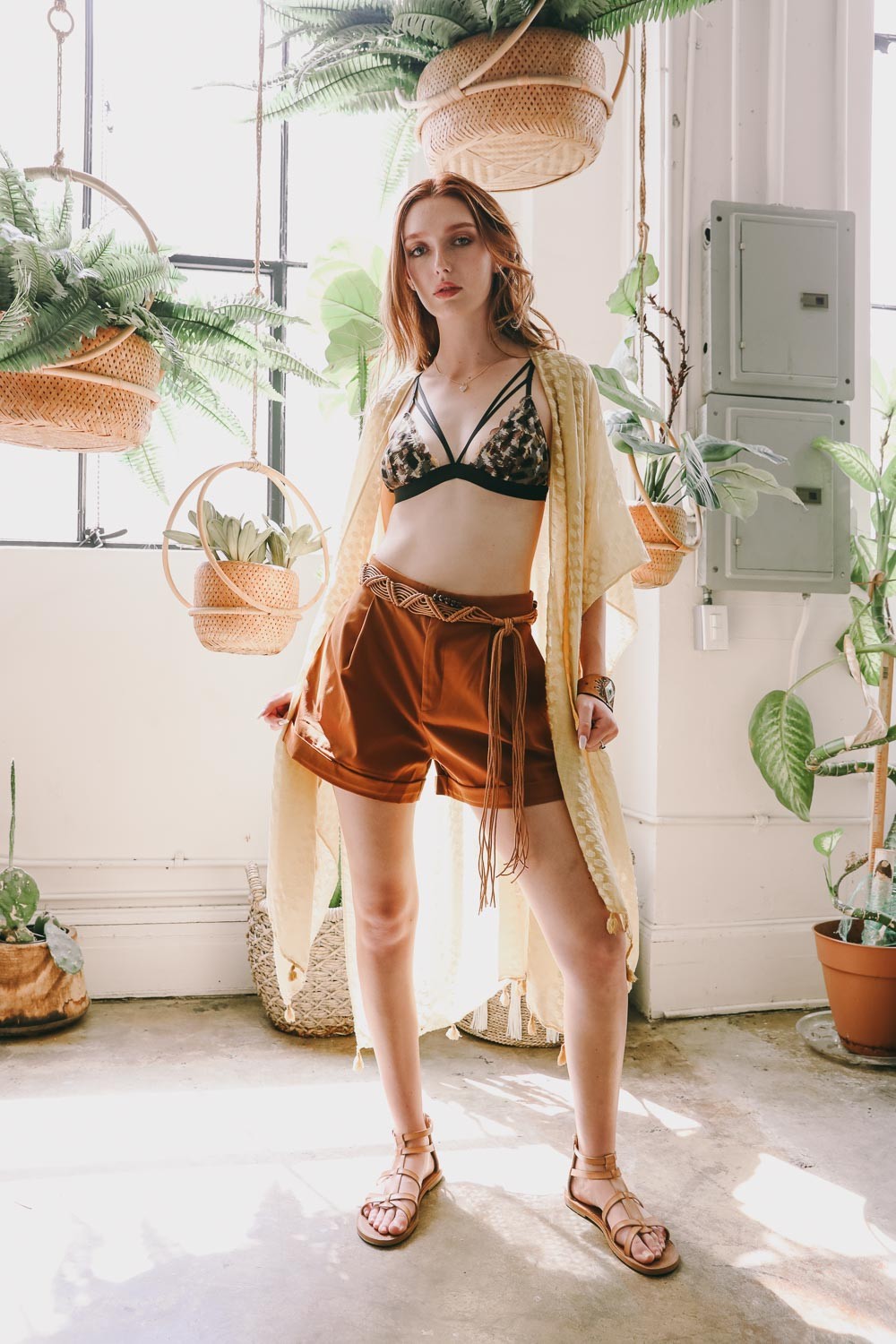 Chic model wearing bohemian braided bead belt over brown shorts and bralette in a stylish indoor setting