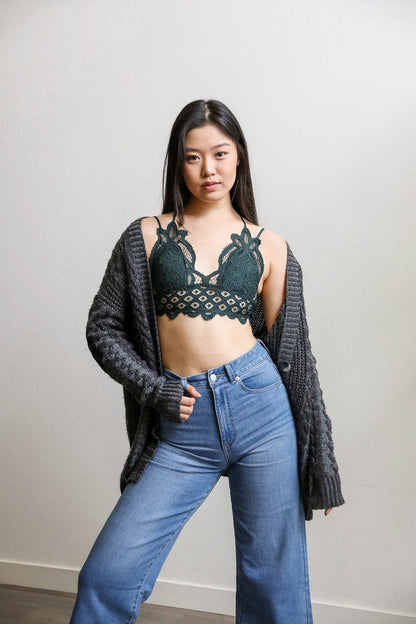 Model wearing a boho crochet bralette in green styled with a gray cardigan and blue jeans