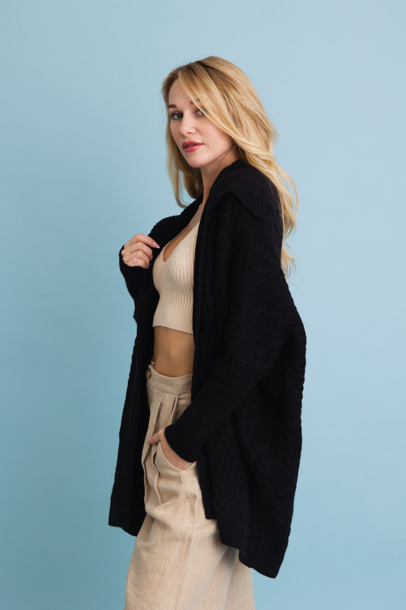 Chunky cable knit poncho cardigan in black worn by a model with casual outfit and relaxed style