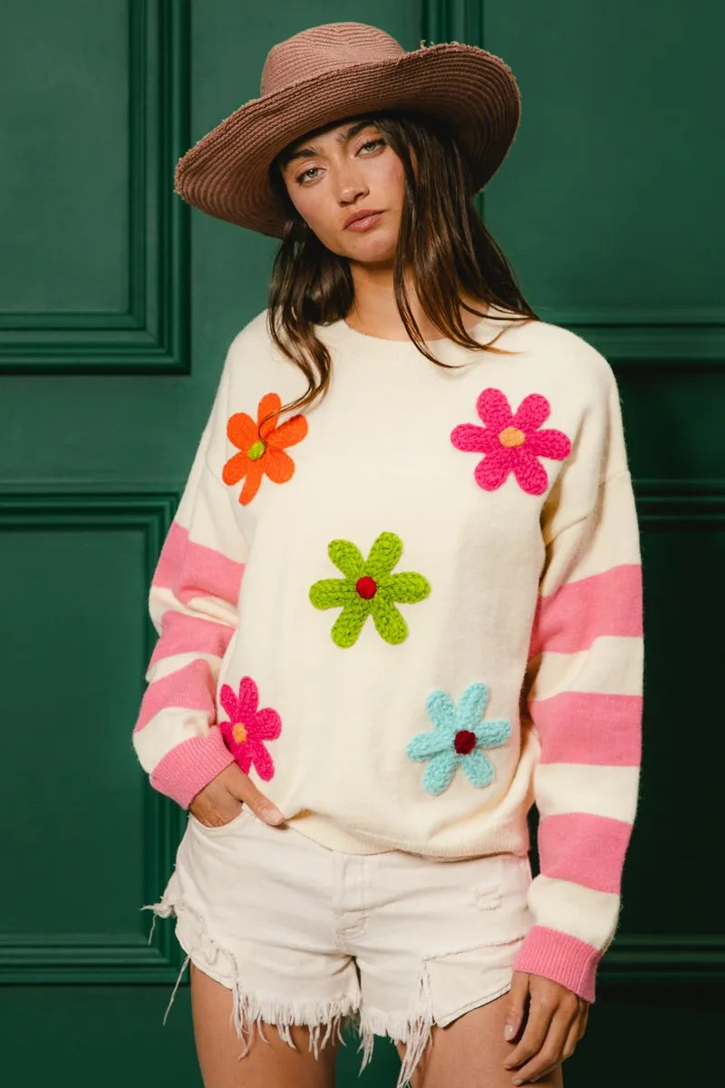 Colorful floral sweater for women featuring vibrant flowers and stripes, paired with a straw hat and shorts
