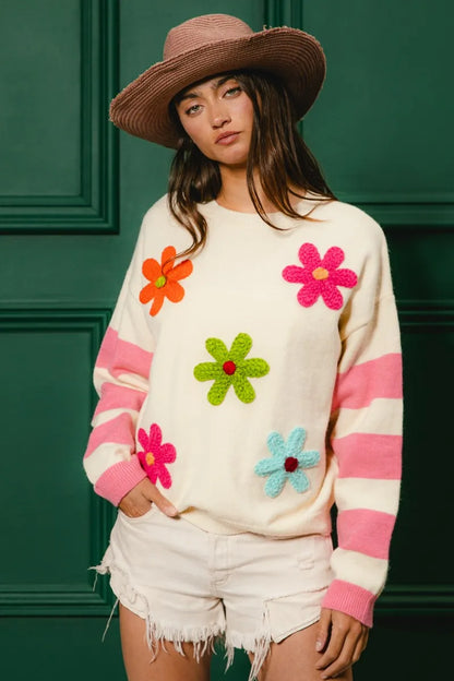 Colorful floral sweater for women featuring vibrant flowers and stripes, paired with a straw hat and shorts
