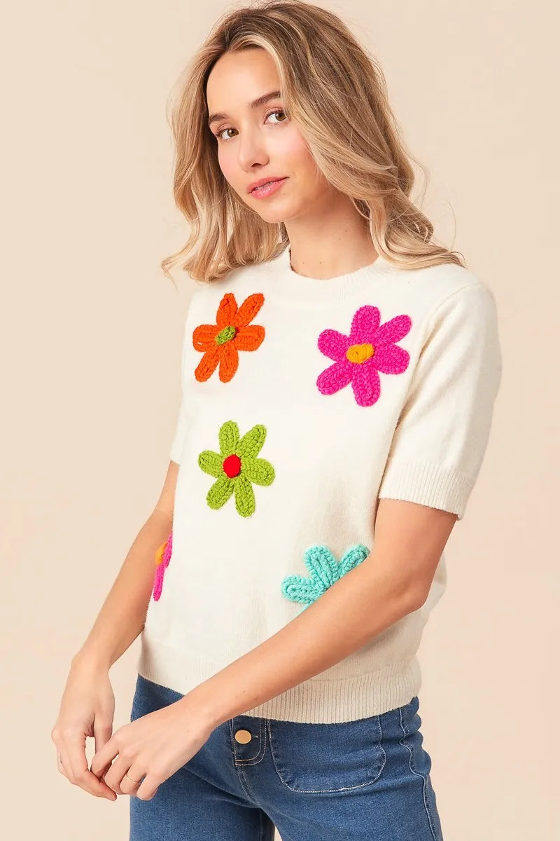 Trendy crochet flower sweater top with colorful floral appliqués on a cream background