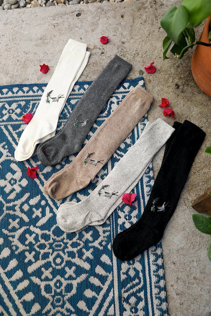 Leto Collection boho knee high socks in various colors with floral embroidery on a patterned rug