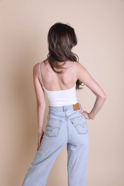 Model wearing a white low back brami top paired with high-waisted jeans from the Leto Collection
