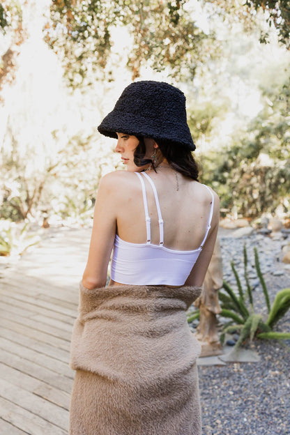 Model wearing an offset shoulder brami top with a bucket hat, standing outdoors in a natural setting