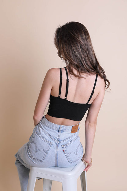 Back view of a woman wearing a black boho offset shoulder brami top paired with high-waisted jeans