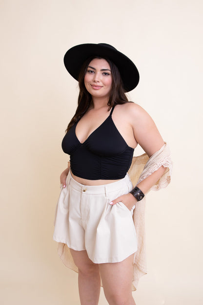 Stylish model wearing a black plus size ruched bralette with high-waisted shorts and a hat