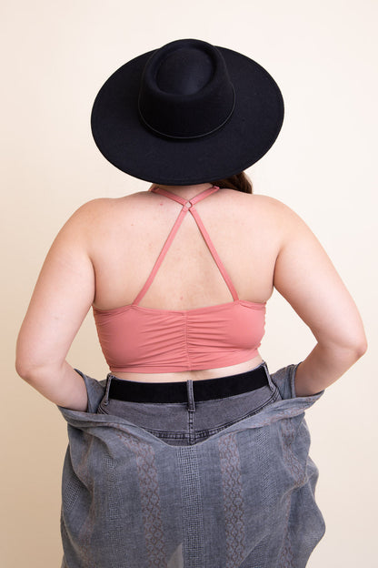Back view of a plus size ruched bralette in dusty rose, paired with a stylish black hat