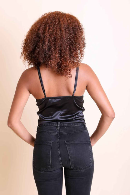 Back view of a woman wearing a black boho satin crop top paired with black jeans.