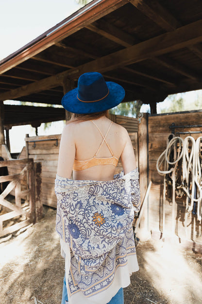 Leto Collection boho tie-dye bralette worn under a blue hat with a patterned shawl in a rustic setting